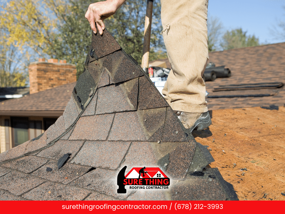 Roofer lifting damaged shingles from a roof in Fayetteville, GA during roof replacement.